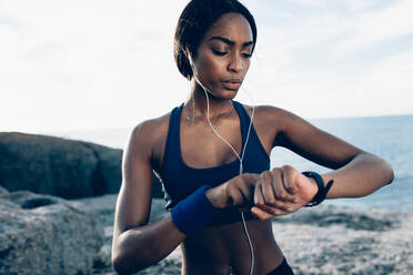 Fit female runner using smart watch to monitor her performance. African Woman setting fitness app on her smartwatch before running session. - JLPSF02695