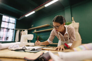 Asiatische Modedesignerin, die eine Skizze zeichnet. Eine Designerin arbeitet in ihrem Modestudio. - JLPSF02735