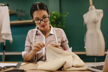 Eine Designerin näht mit der Hand ein Kleid in einem Modeatelier. Eine asiatische Schneiderin arbeitet in ihrer Werkstatt. - JLPSF02751