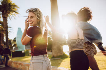 Fröhliche junge Frau, die an einem sonnigen Tag mit ihren Freunden im Park spazieren geht. Gruppe von Freunden, die sich in einem öffentlichen Park vergnügen. - JLPSF02763