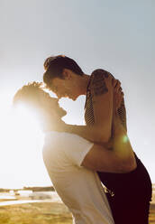 Young couple in love looking at each other and smiling. Man lifting his beautiful girlfriend outdoors in a summer day. - JLPSF02766