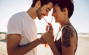 Junges glückliches Paar im Freien, das ein kaltes Getränk aus einer Glasflasche mit Strohhalm trinkt. Seitenansicht von Mann und Frau, die ein Erfrischungsgetränk trinken und lächeln. - JLPSF02773