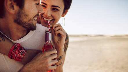 Paar im Urlaub, das sich im Freien vergnügt; Mann nimmt seine Freundin Huckepack und trinkt ein Getränk aus einer Glasflasche. - JLPSF02775