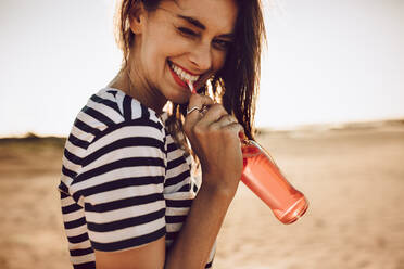 Porträt einer fröhlichen jungen Frau, die ein Getränk mit Strohhalm aus einer Glasflasche trinkt. Mädchen, das an einem Sommertag im Freien eine Limonade trinkt. - JLPSF02780