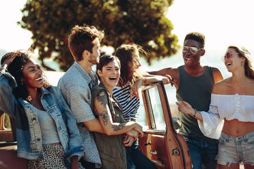 Eine Gruppe von Männern und Frauen auf einem Roadtrip, die am Auto stehen und Spaß haben. Fröhliche Freunde, die sich im Urlaub amüsieren. - JLPSF02802