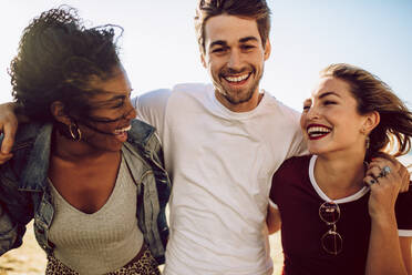 Porträt von drei jungen Freunden, die zusammen im Freien spazieren gehen und lächeln. Gruppe von Männern und Frauen, die Spaß im Freien haben. - JLPSF02806
