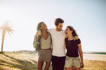 Small group of young people walking together outdoors and smiling. Young man with female friends walking outside on summer day. - JLPSF02807