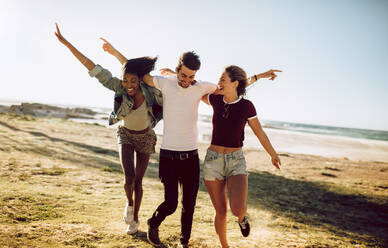 Eine Gruppe von drei jungen Freunden, die mit ausgestreckten Armen zusammen laufen. Ein junger Mann und eine Frau genießen einen Sommertag im Freien. - JLPSF02809