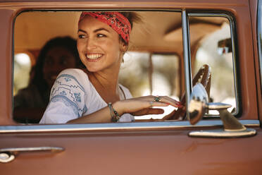 Attraktive Frau, die während der Fahrt aus dem Autofenster schaut. Lächelnde Frau auf Road Trip mit Freunden. - JLPSF02817