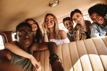 Junger afrikanischer Mann macht Selfie mit Freunden im Auto sitzend. Gruppe von Freunden auf Road Trip macht Selfie. - JLPSF02828