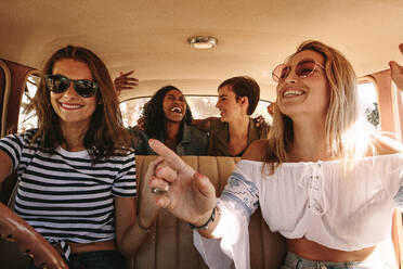 Junge Frauen auf einem Roadtrip, die mit dem Auto unterwegs sind und lachen. Gruppe von gemischtrassigen Frauen, die Spaß auf einem Roadtrip haben. - JLPSF02833