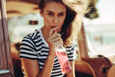 Junge kaukasische Frau, die ein Getränk mit einem Strohhalm aus einer Glasflasche trinkt. Eine Frau trinkt ein erfrischendes Softdrink im Auto. - JLPSF02837
