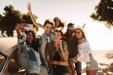 Gruppe von jungen Männern und Frauen genießen auf Road Trip stehen durch das Auto und nehmen selfie. Multirassische Gruppe von Freunden, die Spaß im Freien nehmen selfie mit Smart Phone. - JLPSF02848