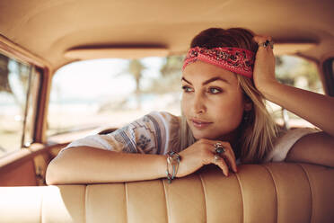 Schöne junge Frau sitzt im Auto und schaut nachdenklich weg. Nachdenkliche Frau mit Kopftuch in einem alten Auto. - JLPSF02878