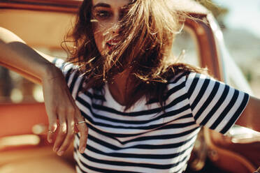 Beautiful young woman standing by the car with hair on her face. Caucasian female on summer vacation. - JLPSF02896