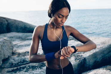 African female runner checking fitness progress on her smart watch. Woman monitoring workout performance on her watch outdoors. - JLPSF02920