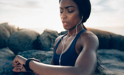 Close up of young fitness woman looking at her smart watch while taking a break from outdoor workout. Sportswoman checking pulse on fitness smart watch device. - JLPSF02921