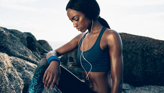 Tired woman with standing outdoors and relaxing after workout. African woman taking break after exercising outdoors. - JLPSF02926