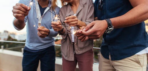 Cropped shot of three people holding sparklers on rooftop. Group of friends enjoying a party with sparklers. - JLPSF02943