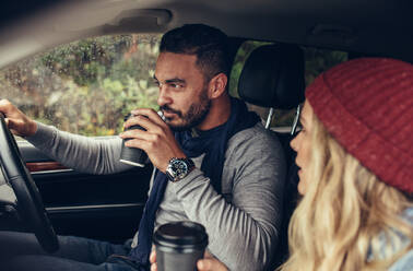 Junger Mann und Frau fahren mit dem Auto und trinken Kaffee. Paar trinkt Kaffee beim Autofahren. - JLPSF02944