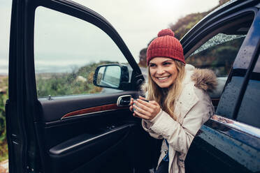Beautiful smiling woman in her car drinking coffee. Happy young female holding cup of coffee and looking away while sitting in her car. - JLPSF02945