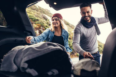 Glückliches Paar auf einer Urlaubsreise, das sein Gepäck aus dem Kofferraum nimmt. Schönes Paar auf einer Autoreise. - JLPSF02947