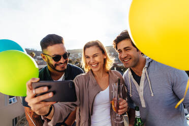 Junge Freunde feiern zusammen ein Selfie machen. Gruppe von Menschen mit Getränken und Luftballons auf einer Dachterrasse Party ein Selfie machen. - JLPSF02972