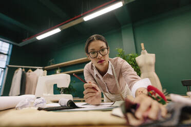 Kreative Designerin bei der Arbeit in ihrem Modeatelier. Asiatische Schneiderin, die an ihrem Arbeitsplatz an Skizzen arbeitet und Stoffe auswählt. - JLPSF03010