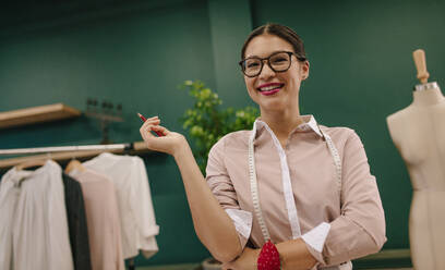 Beautiful young dressmaker standing in workshop and smiling. Happy attractive fashion designer standing in her creative studio. - JLPSF03011