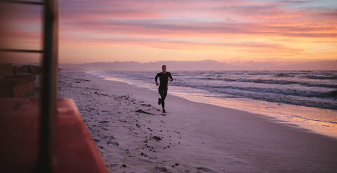 Ein Mann trainiert am Morgen am Strand. Ein gesunder männlicher Sportler läuft am Morgen draußen am Meer. - JLPSF03016