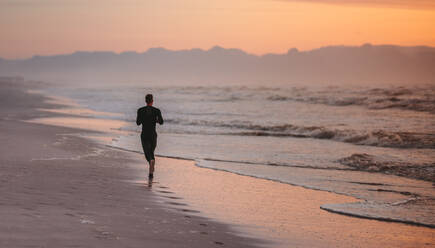 Rückansicht eines Mannes, der am Morgen am Strand läuft. Männlicher Sportler beim Morgenlauf im Freien am Meeresufer. - JLPSF03019