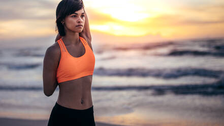 Woman runner stretching hands at the beach. Female athlete warming up before a run in morning at the beach. - JLPSF03021