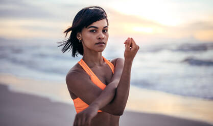 Entschlossene Frau, die ihre Arme streckt und am Strand trainiert. Sportler beim Aufwärmtraining am Meer. - JLPSF03022