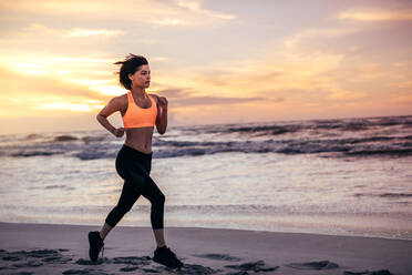 Woman athlete running along the beach in the morning. Woman in running outfit sprinting on the sea shore. - JLPSF03023