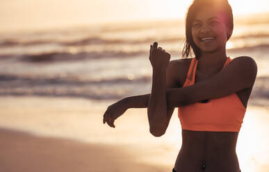 Lächelnde Frau, die ihre Arme am Meer ausstreckt. Weibliche Athletin beim Aufwärmtraining am Strand. - JLPSF03025