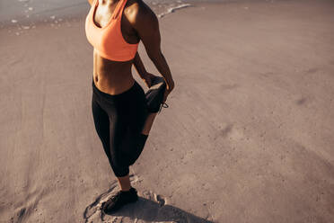 Sportlerin in Sportkleidung beim Dehnen vor dem Laufen am Strand, Ausschnitt: Frau beim Aufwärmen. - JLPSF03030