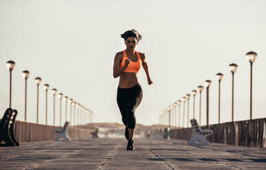 Eine Frau läuft auf der Strandpromenade. Eine fitte Sportlerin sprintet auf der Strandpromenade am Morgen. - JLPSF03033