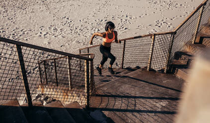 Athletic woman runs up the steps on the beach. Athlete in sportswear training on concrete steps. - JLPSF03034