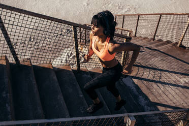 Fitness woman running up the stairway along the beach. Female athlete exercising outdoors in morning. - JLPSF03035