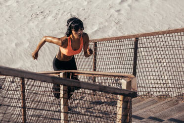 Fitte Frau trainiert auf der Treppe am Strand. Junge Läuferin klettert die Stufen am Strand hinauf. - JLPSF03036