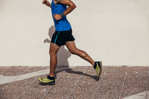 Niedriger Ausschnitt eines sportlichen Mannes, der im Freien auf dem Bürgersteig joggt. Ein Mann in Sportkleidung läuft am Morgen. - JLPSF03041