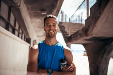 Porträt eines muskulösen Mannes, der im Freien steht und in die Kamera lächelt. Ein Sportler macht nach dem Training eine Pause. - JLPSF03045