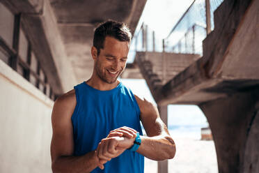 Smiling man using a smartwatch to monitor his progress. Male athlete checking his performance on fitness app on his smartwatch.. - JLPSF03046