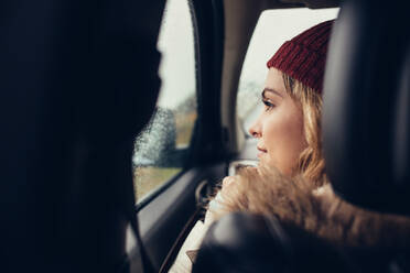 Rear view shot of young woman sitting inside the car and looking outside the window. Caucasian female on a road tip traveling by car. - JLPSF03050