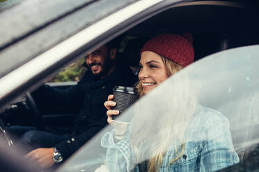 Lächelnde Frau trinkt einen Kaffee mit einem Mann, der das Auto fährt. Junges Paar auf einer Autoreise. - JLPSF03052