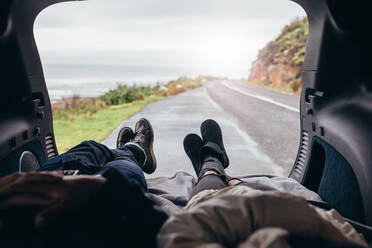 POV-Aufnahme eines Paares, das im Kofferraum eines Autos liegt. Mann und Frau entspannen sich im Kofferraum eines Autos an der Straße. - JLPSF03056
