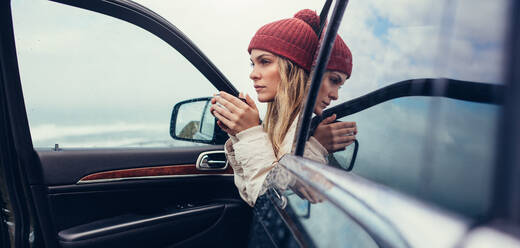 Beautiful young female with coffee in hand sitting in a car. Female on road trip drinking coffee inside car. - JLPSF03062