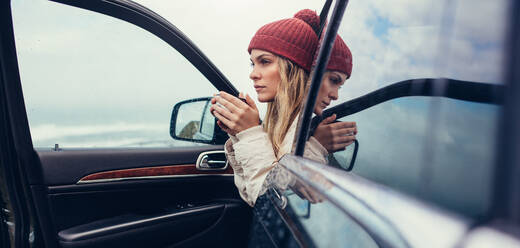 Schöne junge Frau mit Kaffee in der Hand im Auto sitzend. Frau auf Road Trip trinkt Kaffee im Auto. - JLPSF03062