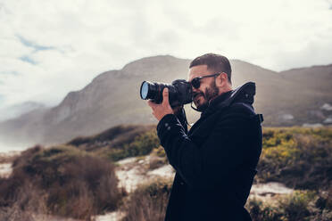 Gutaussehender Mann mit Digitalkamera im Freien. Junger männlicher Fotograf beim Fotografieren in der Natur an einem Wintertag. - JLPSF03075