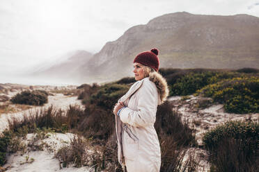 Seitenporträt einer Frau in Winterkleidung, die im Freien am Strand steht. Frau im Winterurlaub mit Blick auf die Aussicht. - JLPSF03082